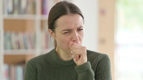 Young Adult Woman Coughing Into Hand Indoors