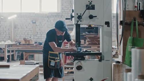 Carpentry Works Worker Cutting Along the Wooden Detail with an Automatic Saw in the Workshop