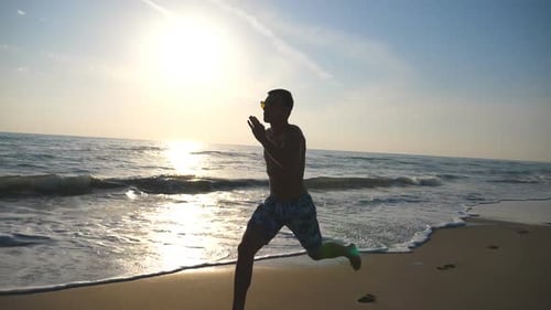 Silhouette of Young Sporty Man Running Fast Along Coast During Sunrise