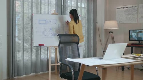 Asian Woman Engineer With A Laptop Drawing Blueprint On The Whiteboard At The Office