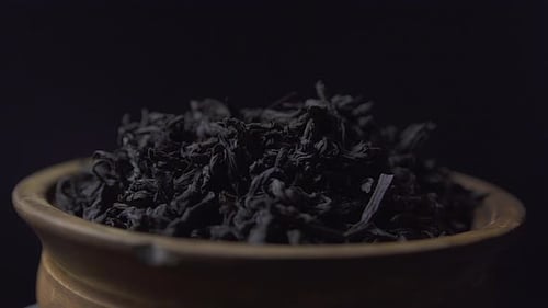Close up view dry black ceylon tea leaves rotate in a clay bowl on black background