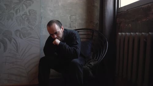 Man Sitting Contemplatively in Dark Modern Interior