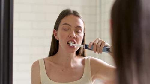 Hermosa mujer cepillándose los dientes mirándose en el espejo