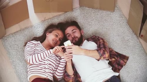 Cheerful Couple Lying on Rug Taking Selfie