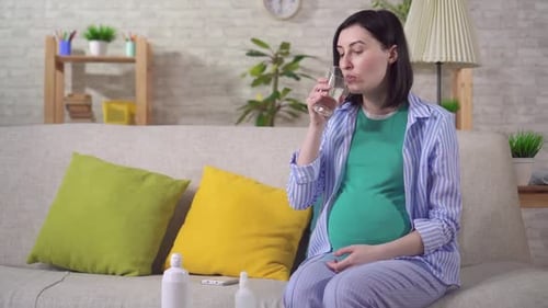 Pregnant Woman Taking Pill on Couch Indoors