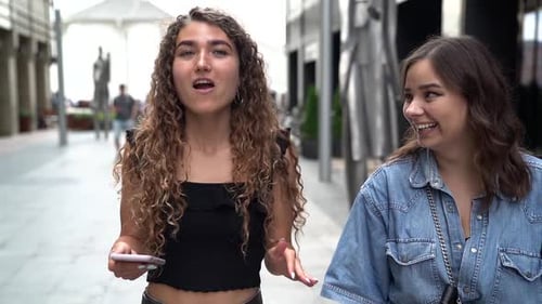 A Friend and a Woman with Curly Hair Walk Around the City in the Summer and Chat While Holding a