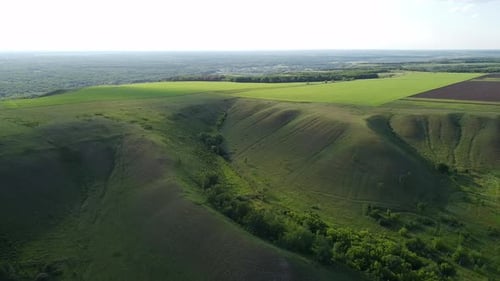 Flight by drone over scenic hills with green forest and farm fields. Aerial view of nature landscape