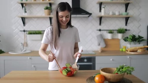 Woman Mixes Salad with Wooden Spoons in Kitchen
