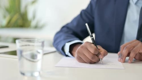 Nahaufnahme der Hände eines afrikanischen Geschäftsmannes, der auf Papier schreibt