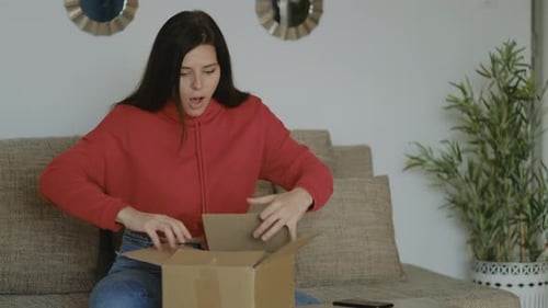 Surprise brunette woman in red hoodie opening online order at home