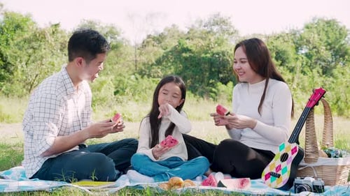 Family Enjoying Picnic Eating Watermelon in Grassy Field