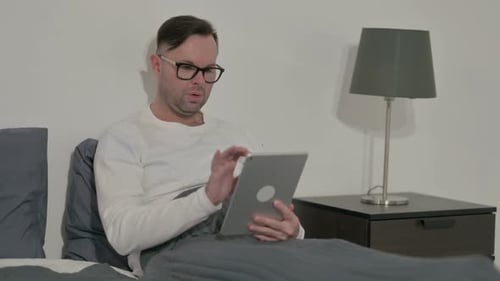 Man Using Tablet in Bed at Home
