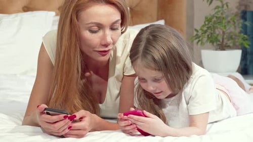 Woman and Child Lying on Bed Using Smartphones