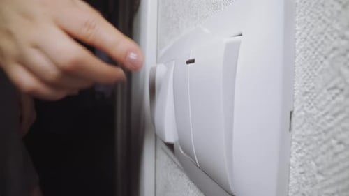 Hand Turning Off White Light Switch on Wall