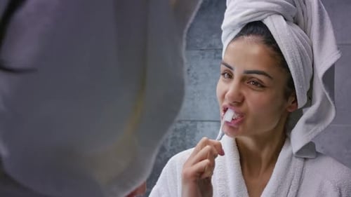 Woman Brushing Teeth in Bathroom Mirror