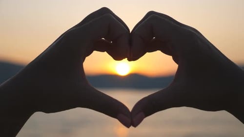 Mujer haciendo su corazón a través de las manos con Golden Sundown de fondo. Silueta de brazos femeninos