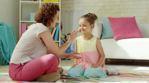 Mère se maquillant à la petite fille mignonne et jouant avec elle