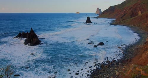Large Waves with Foam Roll on Hilly Ocean Rocky Beach at Sunset
