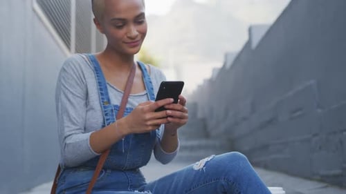 Mixed race woman using smartphone sitting on outdoor stairs