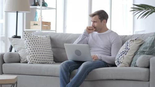 Man Coughing While Using Laptop on Gray Couch