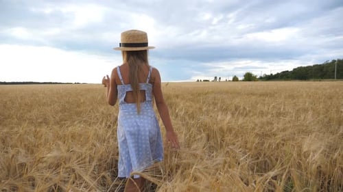 Petite fille au chapeau de paille marchant dans le champ de blé, se tournant vers la caméra et souriant