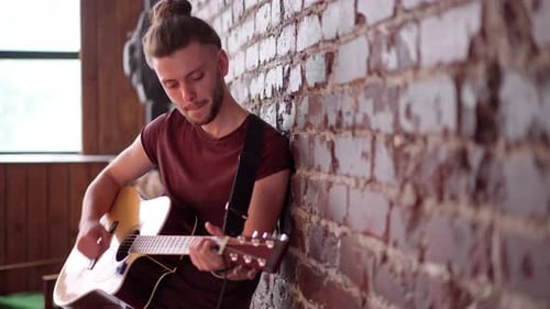 Man Plays Guitar and Sings Indoors by Brick Wall