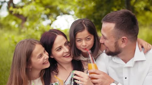 Smiling Father Mother and Two Cute Daughters Drinking Fresh Juice at Green