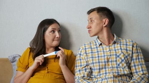 Frau zeigt einem Mann das Ergebnis eines Schwangerschaftstests, während sie im Bett sitzt, Überraschung, Nachdenklichkeit