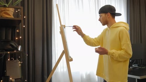 Young Adult Painting on Canvas in Brightly Lit Room