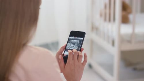 Woman Viewing Ultrasound on Mobile Phone Near Crib