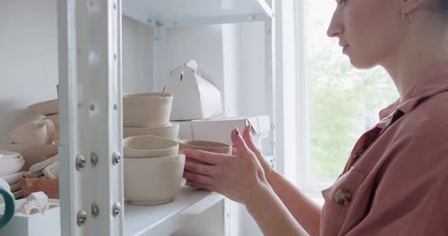 Woman Arranging Handmade Pottery in Bright Studio