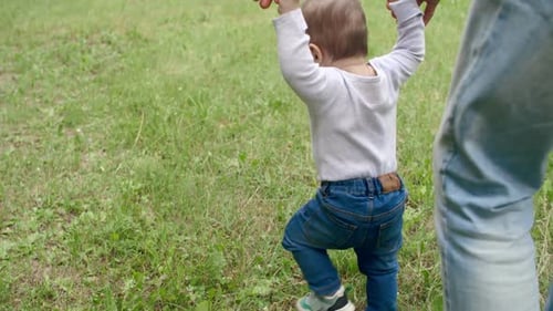 Infant Taking First Steps with Parent on Grass