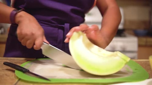 Gros plan sur une femme noire coupant un melon miellat en tranches