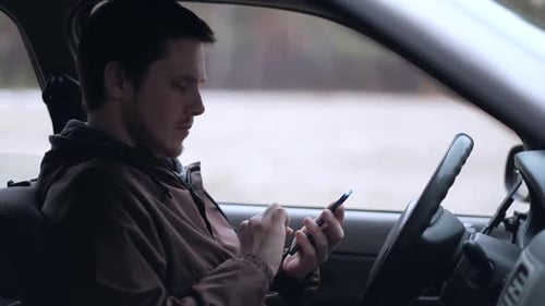 Man Uses Smartphone in Car on City Street