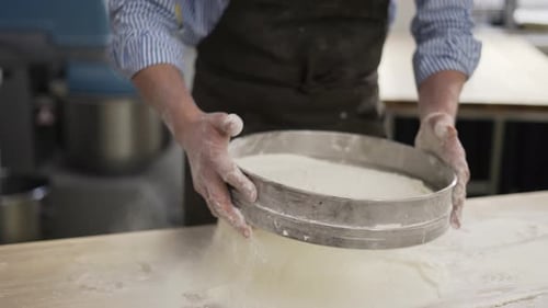 Baker Sifting Flour with a Sieve on Table