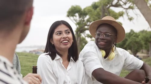 Jeune femme latino-américaine et homme africain avec des amis assis par terre en train de s'amuser à