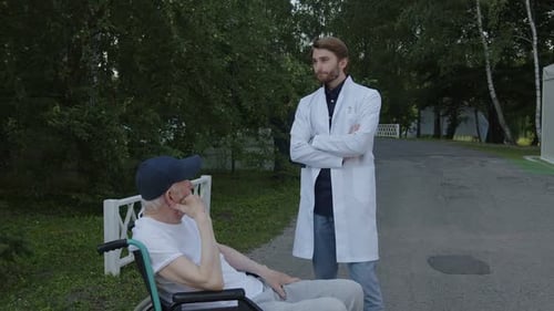 Doctor Talking to Senior Man in Wheelchair Outdoors