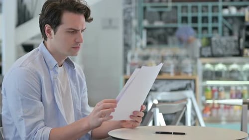 Young Adult Reviews Documents in Cafe Meeting