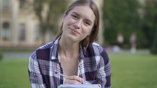 Cheerful Student Studying on Campus Lawn, Smiling