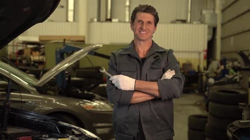 Waist up portrait view of the auto mechanic man standing arms crossed with wrench at workshop