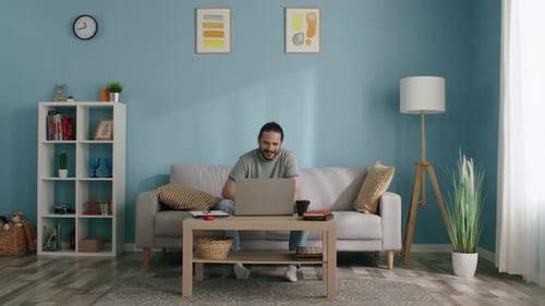 Young Adult Waving at Laptop on Couch