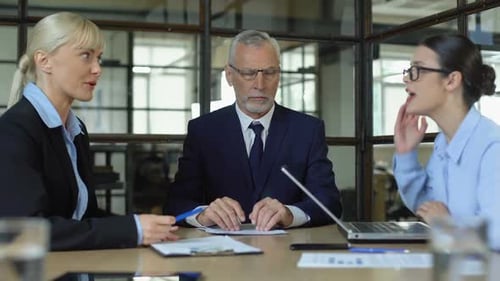 Elderly CEO Meditating to Reduce Stress While Female Workers Arguing in Office
