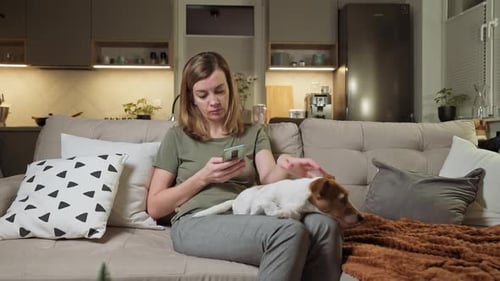 Woman Using Smartphone with Dog on Couch