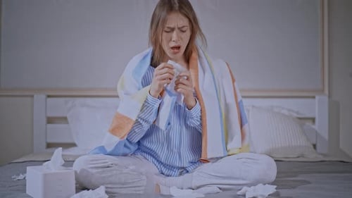 Woman with a Cold Blowing Her Nose on Bed