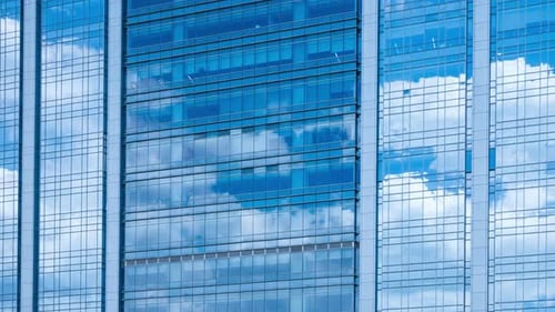 Zeitraffer, Blick auf einen glasbedeckten Wolkenkratzer, der den blauen Himmel und vorbeiziehende Wolken reflektiert