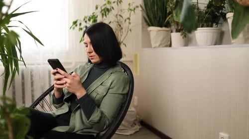 Woman Uses Smartphone Sitting Among Potted Plants