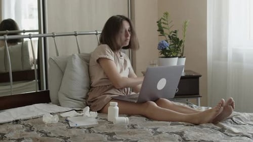 Woman Checks Thermometer and Takes Pills in Bed
