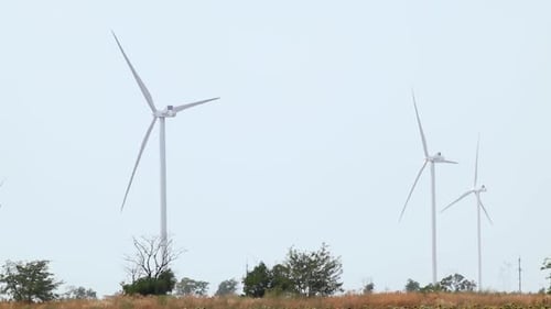 Wind generators rotate on grey sky in field