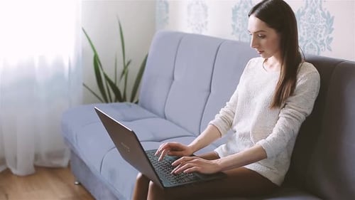 Woman Typing on Laptop Sitting on Couch Indoors