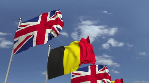 Waving Flags of United Kingdom and Belgium Against Blue Sky